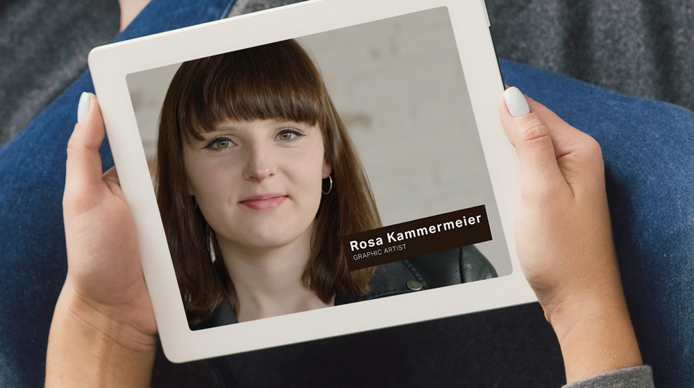 Tablet displays woman’s portrait with her name and title in the lower third right hand corner.
