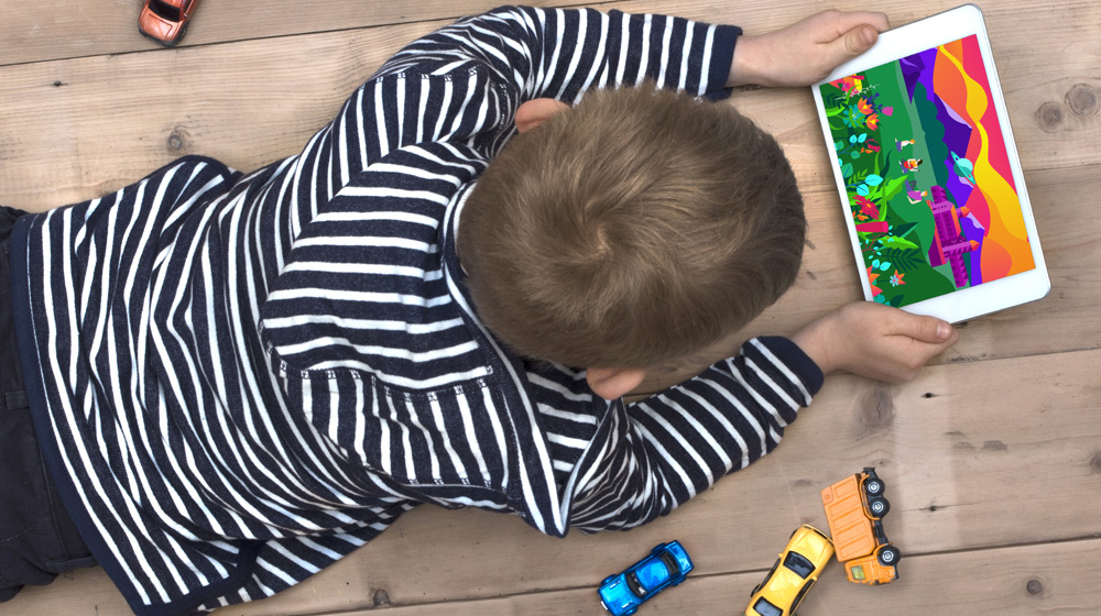 Boy laying on the floor holding a tablet with a colorful game about space.