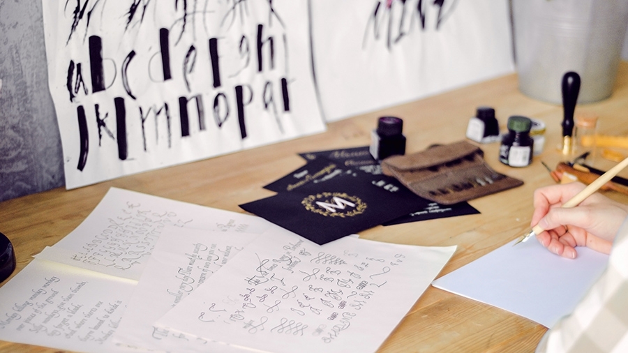 A person is practicing lettering on paper at a desk with a modern quill and ink A person is practicing lettering on paper at a desk with a modern quill and ink