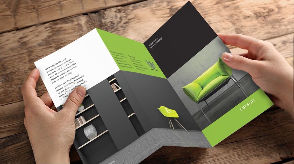 Woman holding black, white, and green trifold brochure for furniture company Woman holding black, white, and green trifold brochure for furniture company