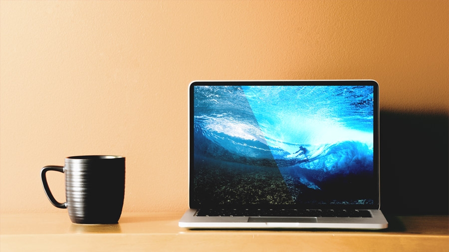 Coffee cup and laptop sitting on pale orange table. Laptop displays underwater view of surfer riding ocean wave Coffee cup and laptop sitting on pale orange table. Laptop displays underwater view of surfer riding ocean wave