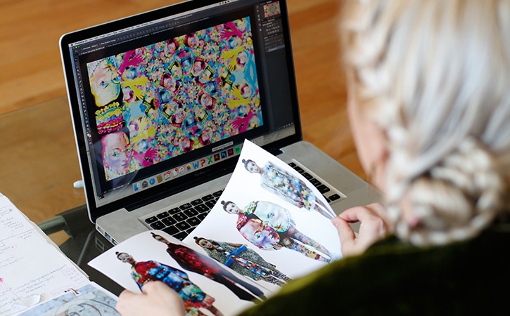 Designer flips through fashion collection magazine while viewing patterned tile in Illustrator.