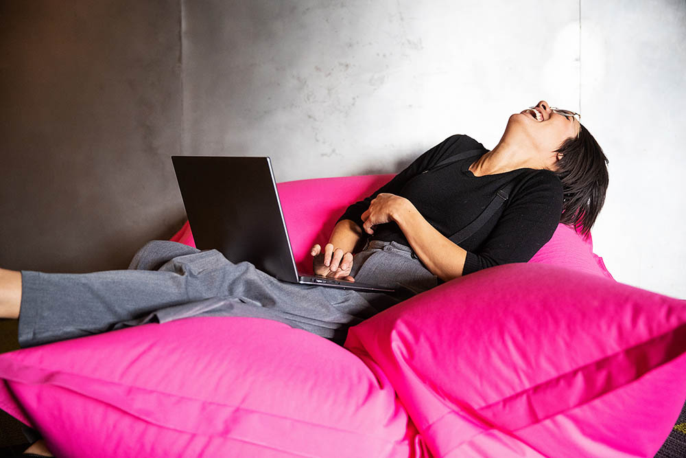 Woman laughing with laptop computer while sitting on pink beanbag chair Woman laughing with laptop computer while sitting on pink beanbag chair