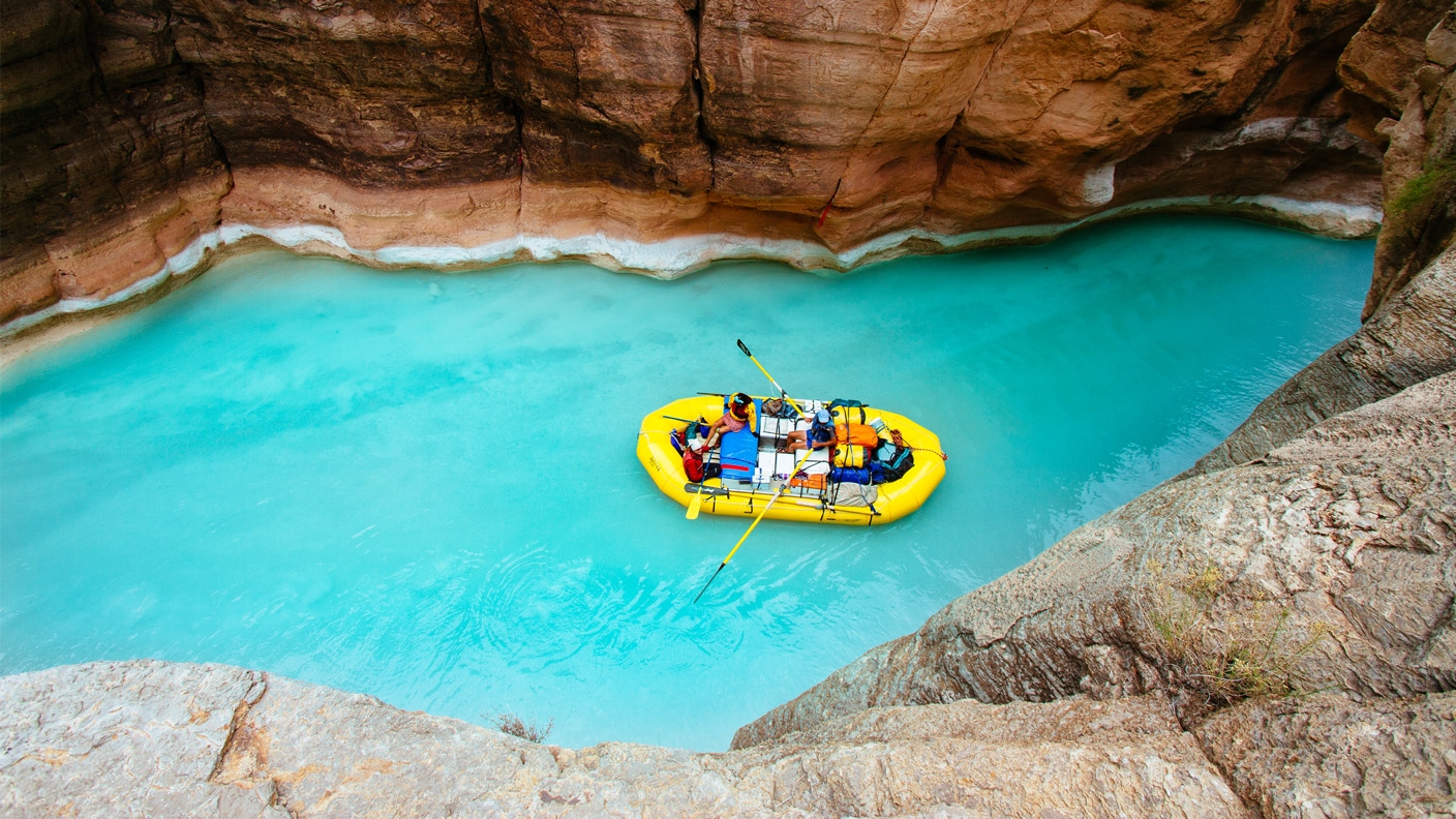 Deux personnes flottant sur un radeau pneumatique entre les parois d’un canyon, sur une eau d’un bleu limpide.